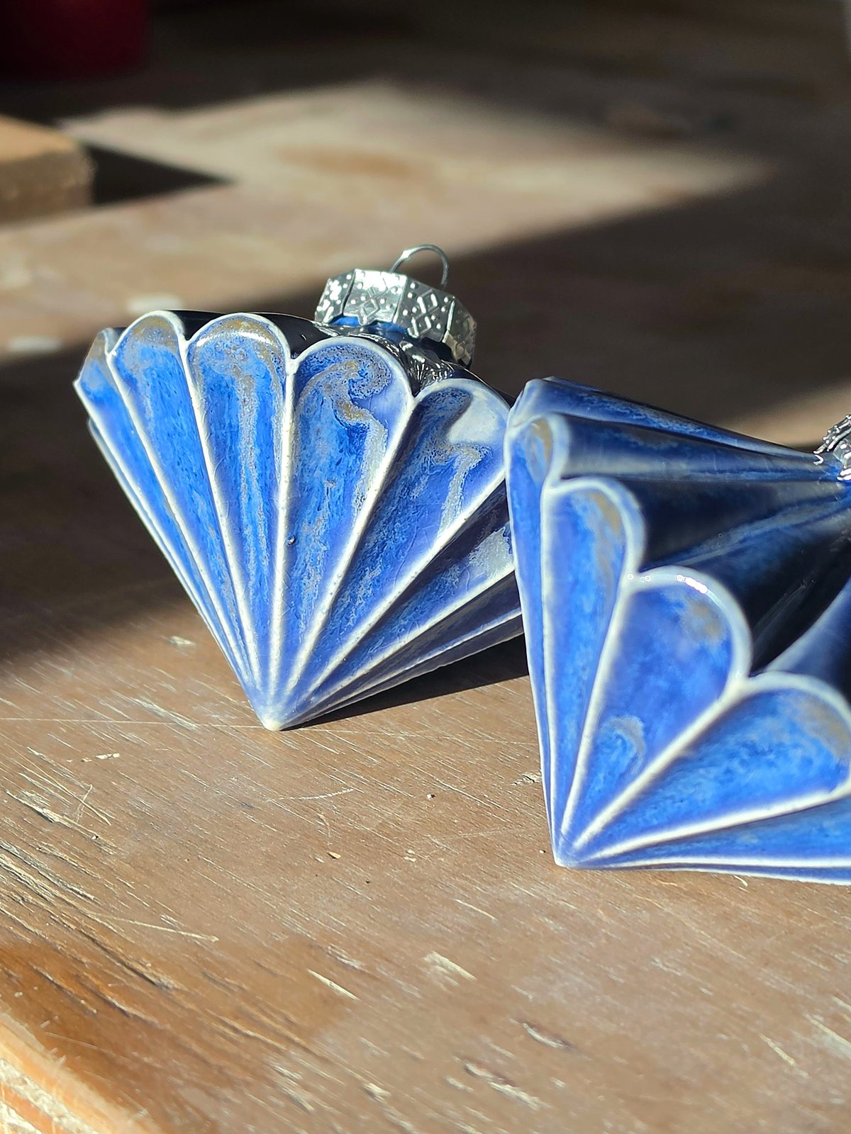 Close side view of two Floating Blue baubles, cobalt pooling in the folds and breaking to white along each ridge.