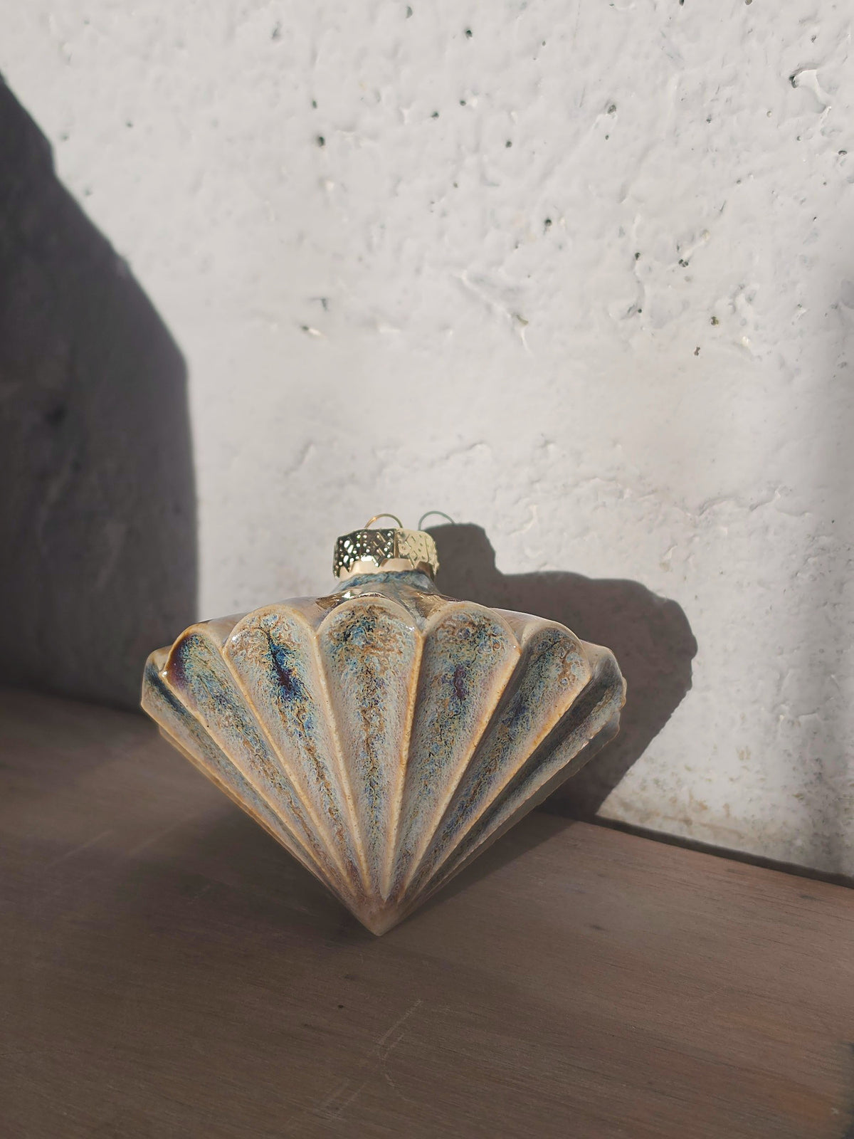 Amber Blue Ribbed Diamond ceramic bauble standing upright against a white wall, fluted fan shape with a gold cap and hook.
