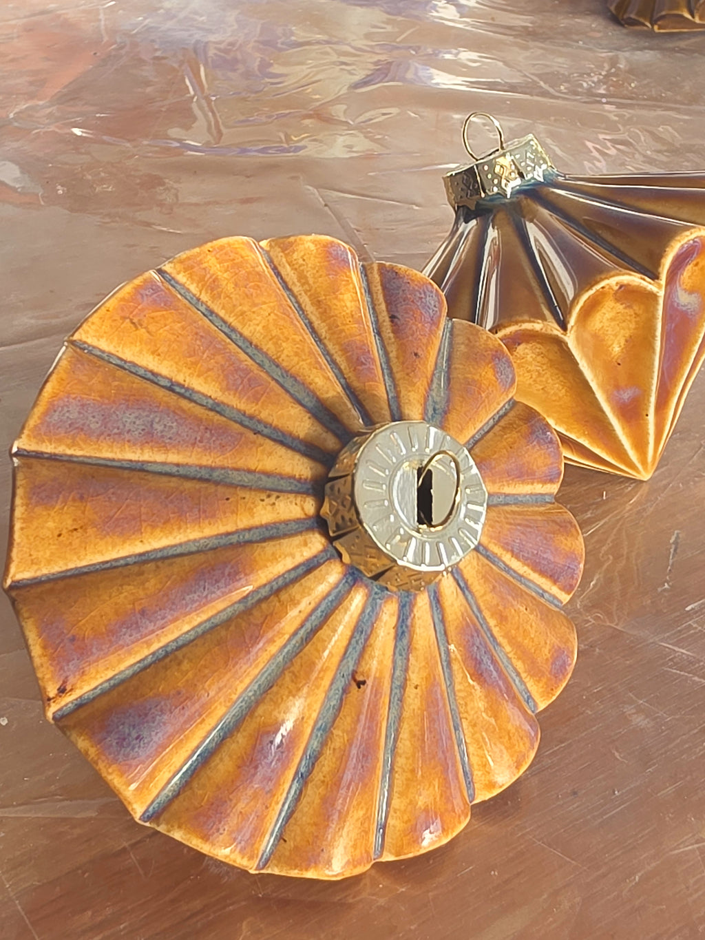 Floating Orange Ribbed Diamond ceramic bauble seen from above, amber orange glaze shading to copper and violet along every ridge around the metal cap.