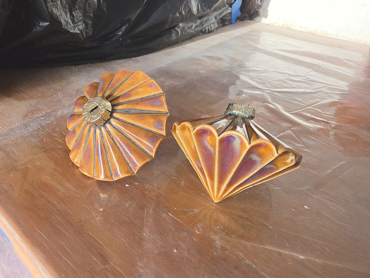 Two Floating Orange Ribbed Diamond ceramic baubles on a bench, one upright and one on its side, glossy orange glaze.