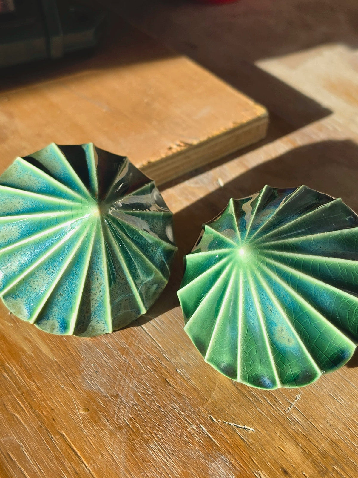 Top view of two green ceramic baubles showing the pleated ridges radiating from the centre.
