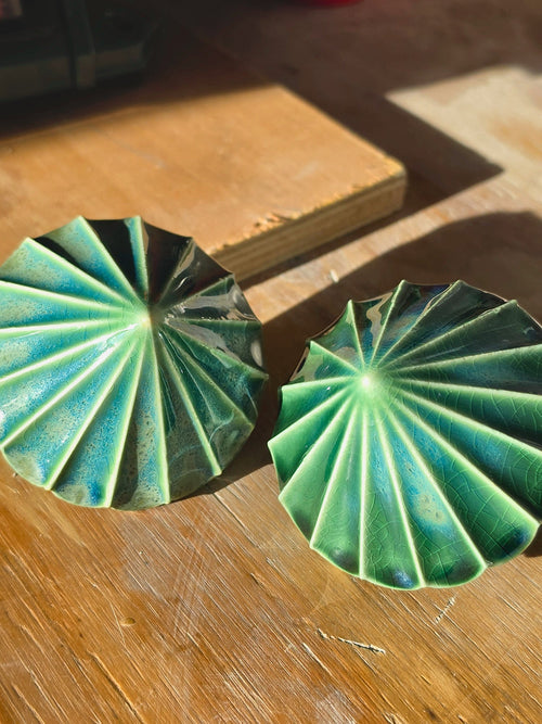 Top view of two green ceramic baubles showing the pleated ridges radiating from the centre.
