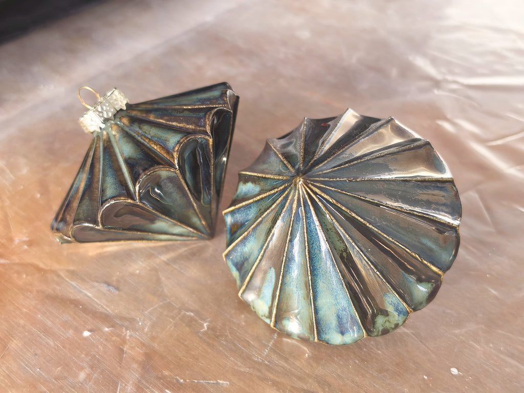 Metallic green Ribbed Diamond ceramic bauble lying on its side, pleated ridges in deep green, teal and bronze glaze.