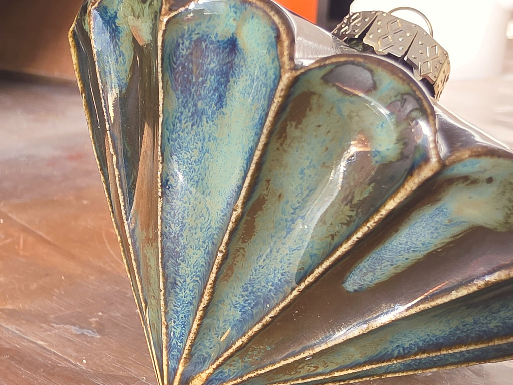 Close view of a metallic green ceramic bauble, glaze shifting from blue and green to bronze along each fluted ridge.