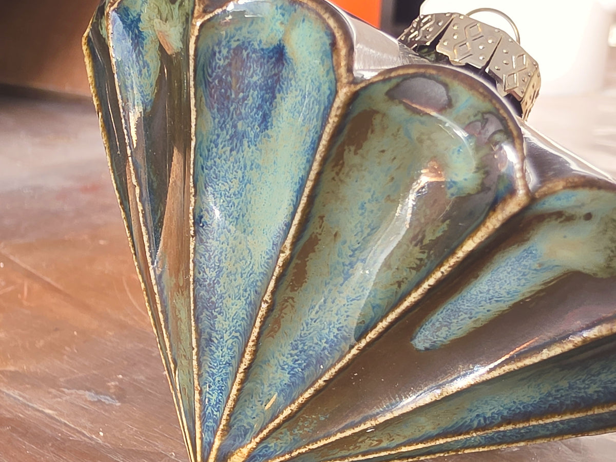 Close view of a metallic green ceramic bauble, glaze shifting from blue and green to bronze along each fluted ridge.