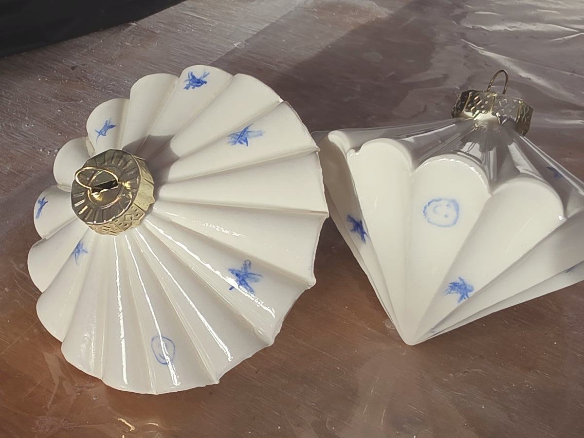 White glossy ceramic bauble seen from above, pleated ridges decorated with small hand drawn blue stars.